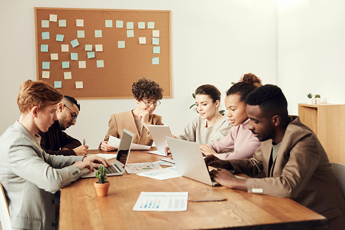 Office workers in a meeting room focused on laptops and documents amid a dispute over a bizarre lunchtime ritual.
