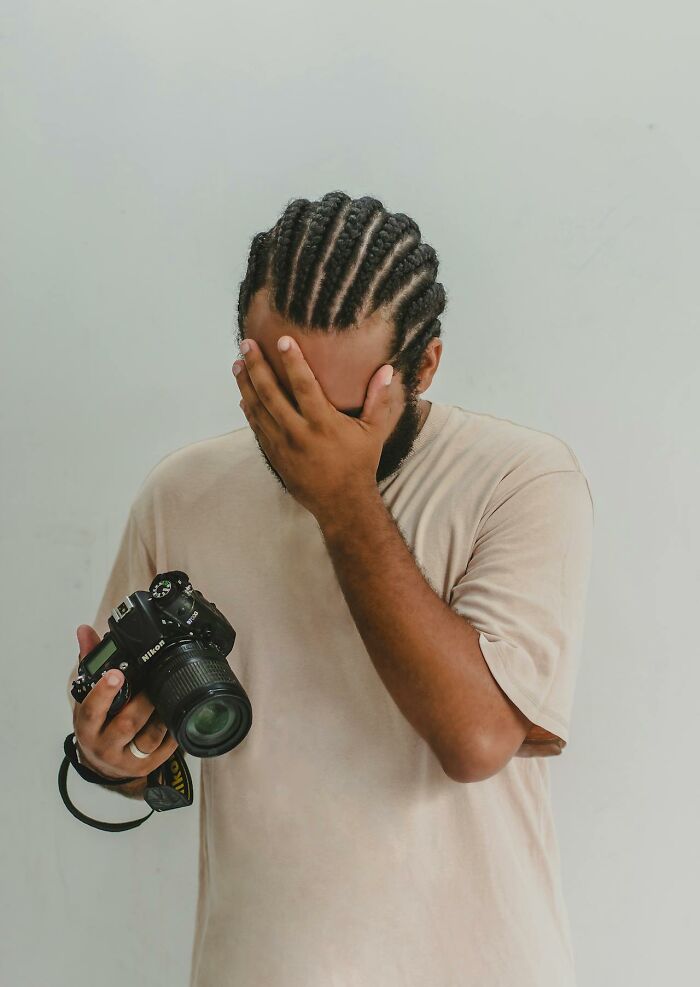 Man with braided hair holding a Nikon camera covering his face, illustrating PR campaign fails and bad decisions.