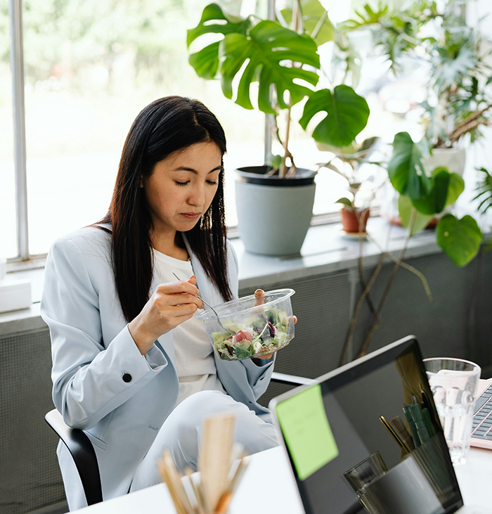 Woman eating salad at office desk during lunch, reflecting on worker confrontation about bizarre lunchtime ritual.