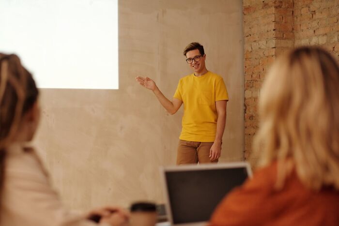 Young man in a yellow shirt presenting to a small audience about PR campaigns and decisions in a modern office setting.