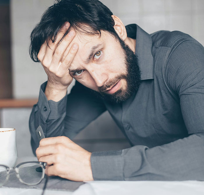 Man looking heartbroken, holding glasses, reflecting on a failed proposal and desire for a rich husband over hardworking partner.