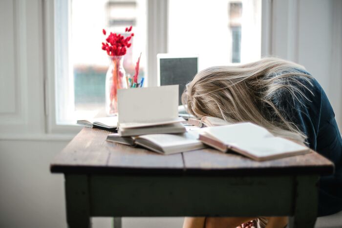 Woman resting her head on a table with books, illustrating frustration from picking the wrong line at the grocery store.