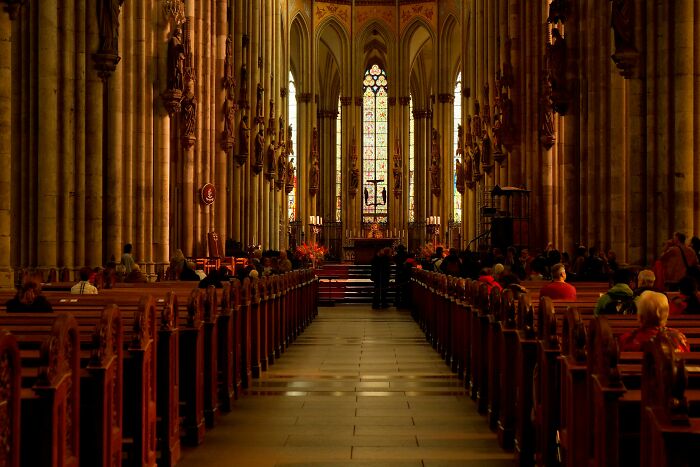 Interior view of a grand cathedral with people seated, highlighting performative behaviors in societal settings.