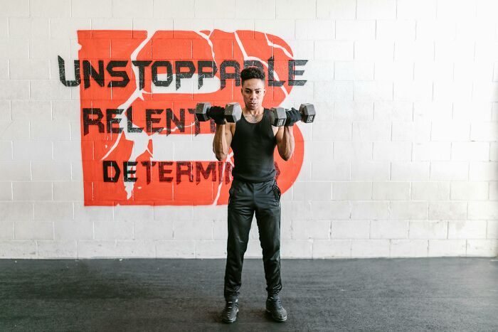 Person lifting dumbbells in a gym with a wall sign about resilience and determination, symbolizing coping with tough times. Person lifting dumbbells in a gym with a wall sign about resilience and determination, symbolizing coping with tough times.