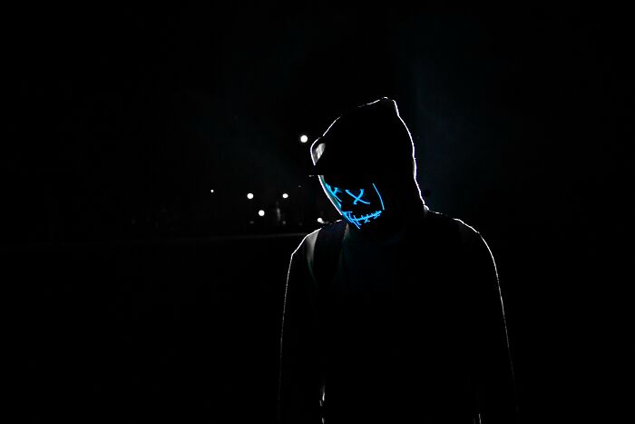 Person wearing a glowing mask in dark hooded outfit representing hidden dark trait and shadow self concept at night. Person wearing a glowing mask in dark hooded outfit representing hidden dark trait and shadow self concept at night.