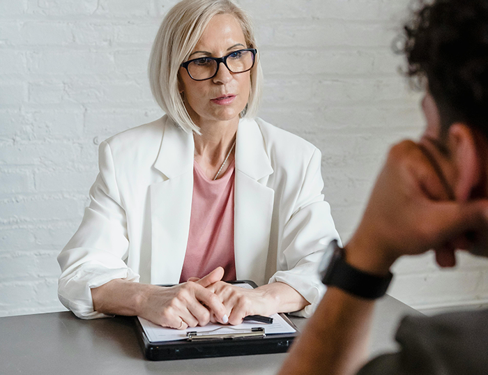 Woman in white blazer disciplinarian worker in a serious discussion with a man at office table about workplace behavior Woman in white blazer disciplinarian worker in a serious discussion with a man at office table about workplace behavior