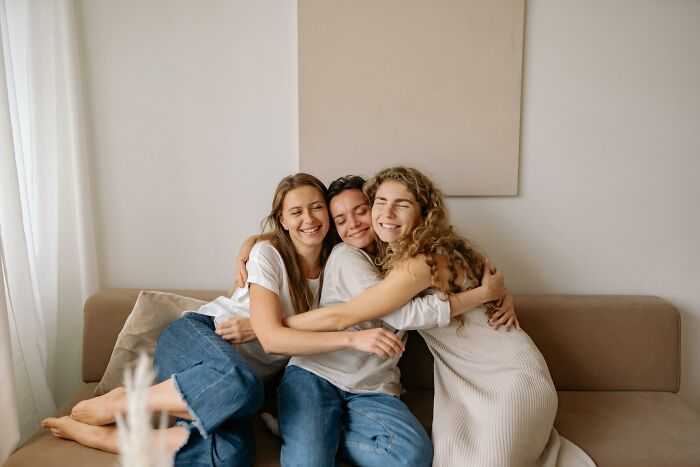 Three friends smiling and hugging on a couch, illustrating moments related to picking the wrong line at the grocery store.