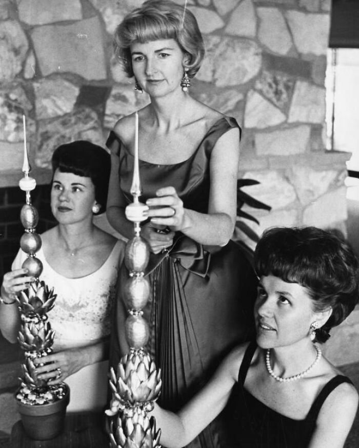 Three LA women in elegant 1960s dresses arranging decorative candles, showcasing classic style and grace.