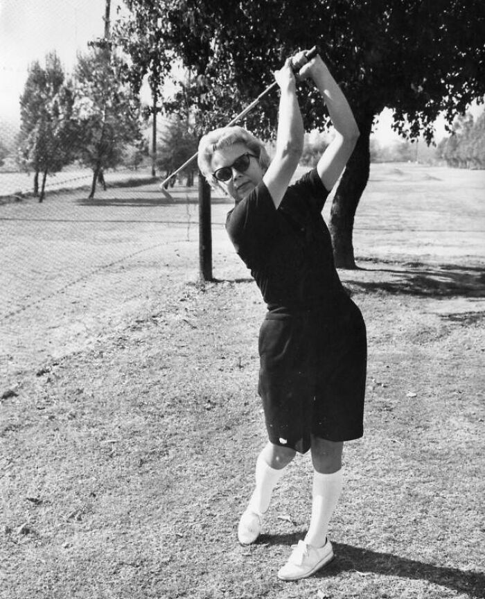 LA woman playing golf outdoors in 1962, wearing sunglasses and vintage sportswear, enjoying life and leisure activities.