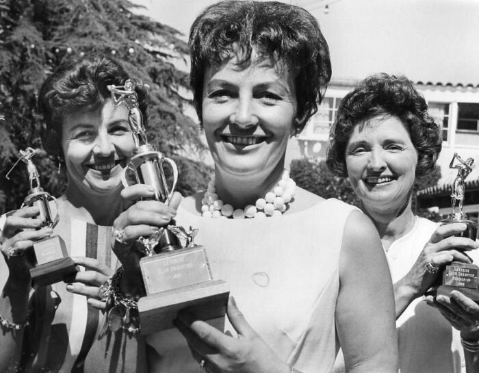 Three smiling LA women in 1962 holding trophies, celebrating success and living their best lives in a sunny outdoor setting.
