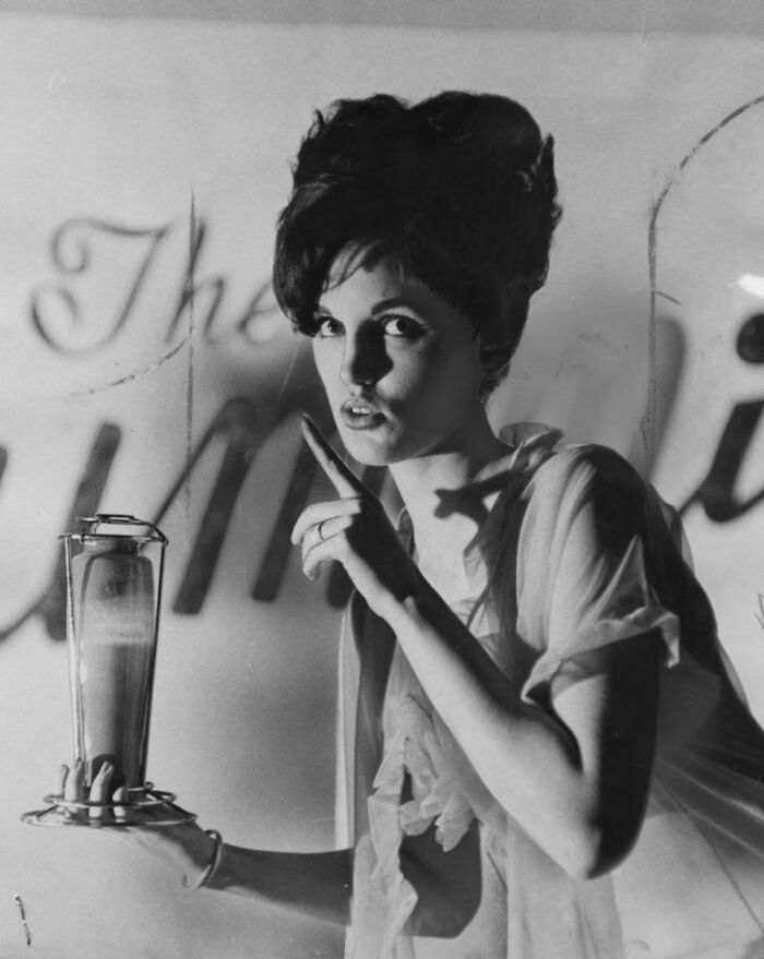 LA woman in 1962 holding a drink, posing with a finger raised, living her best life in Black and white vintage photo.