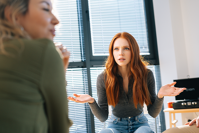 Young woman with red hair explaining and gesturing while discussing friend’s boyfriend’s comment about body count in a bright room. Young woman with red hair explaining and gesturing while discussing friend’s boyfriend’s comment about body count in a bright room.