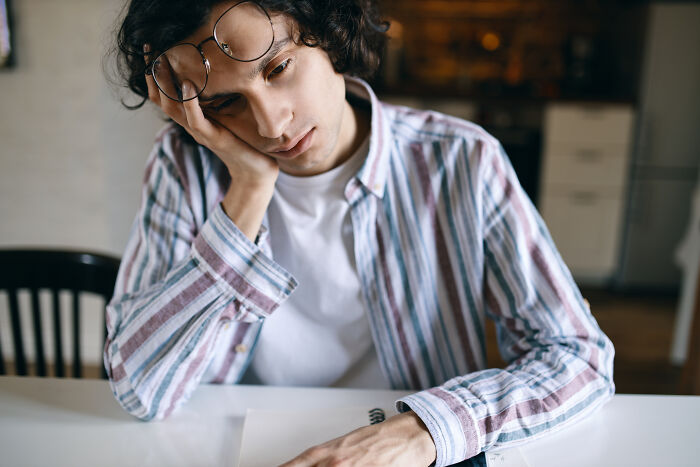 Young person with glasses resting head on hand, looking thoughtful while writing and exploring words that don’t exist in English.