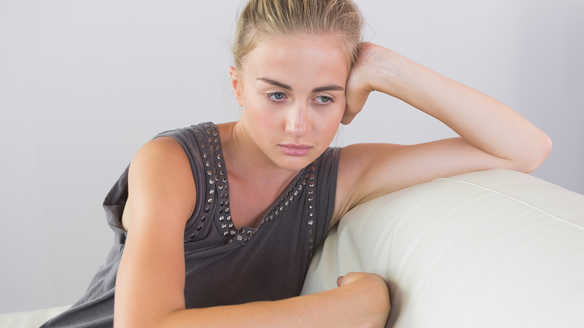Young woman looking pensive and sad on a white couch, reflecting on estranged dad with cancer seeking to reconnect.