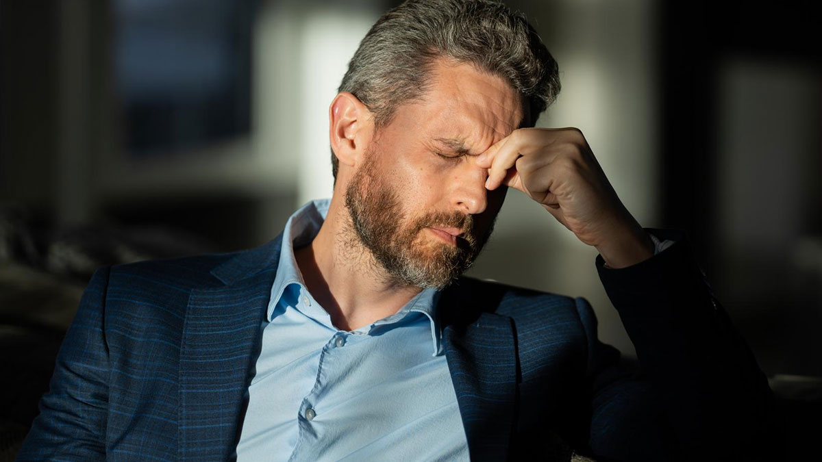Stressed man in blue suit pinching bridge of nose, depicting tension after girlfriend lays down ultimatum.