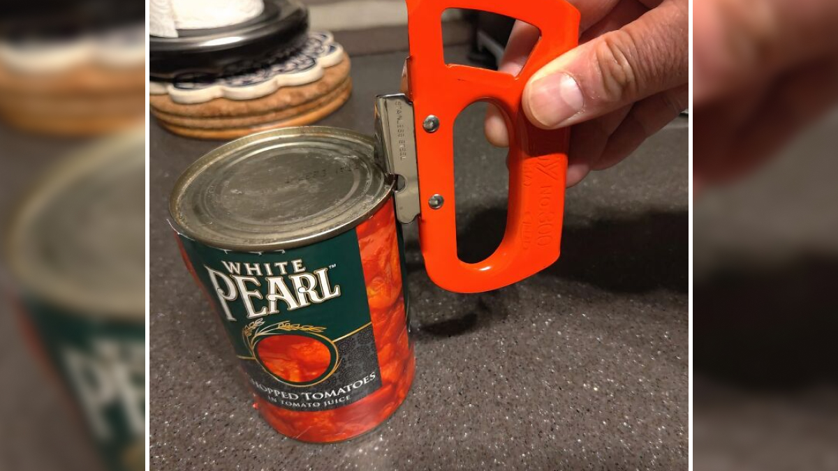 Hand using a durable can opener to open a can of White Pearl chopped tomatoes on a kitchen counter.
