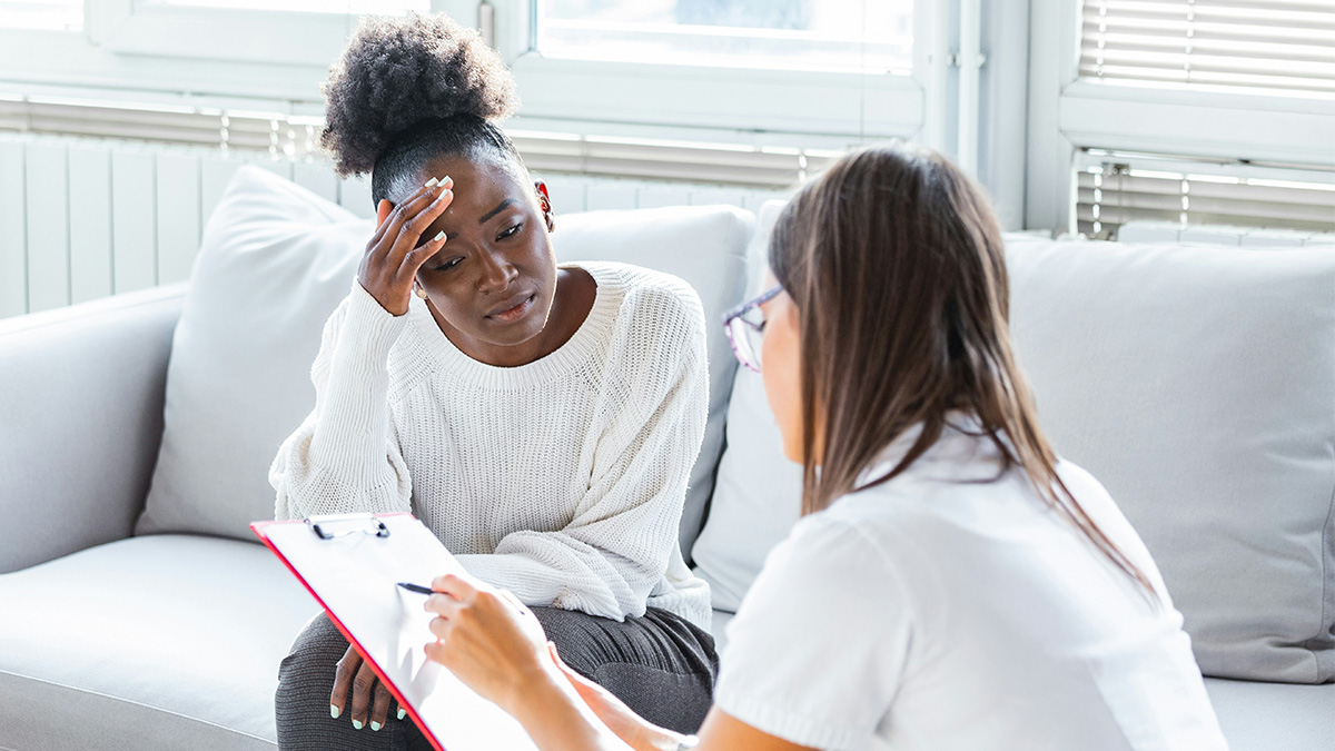 Woman looking confused during a psychiatrist session while the psychiatrist takes notes on a clipboard in a bright office.