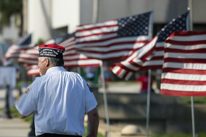 Veteran standing near a row of American flags, highlighting themes of performative behaviors in society.