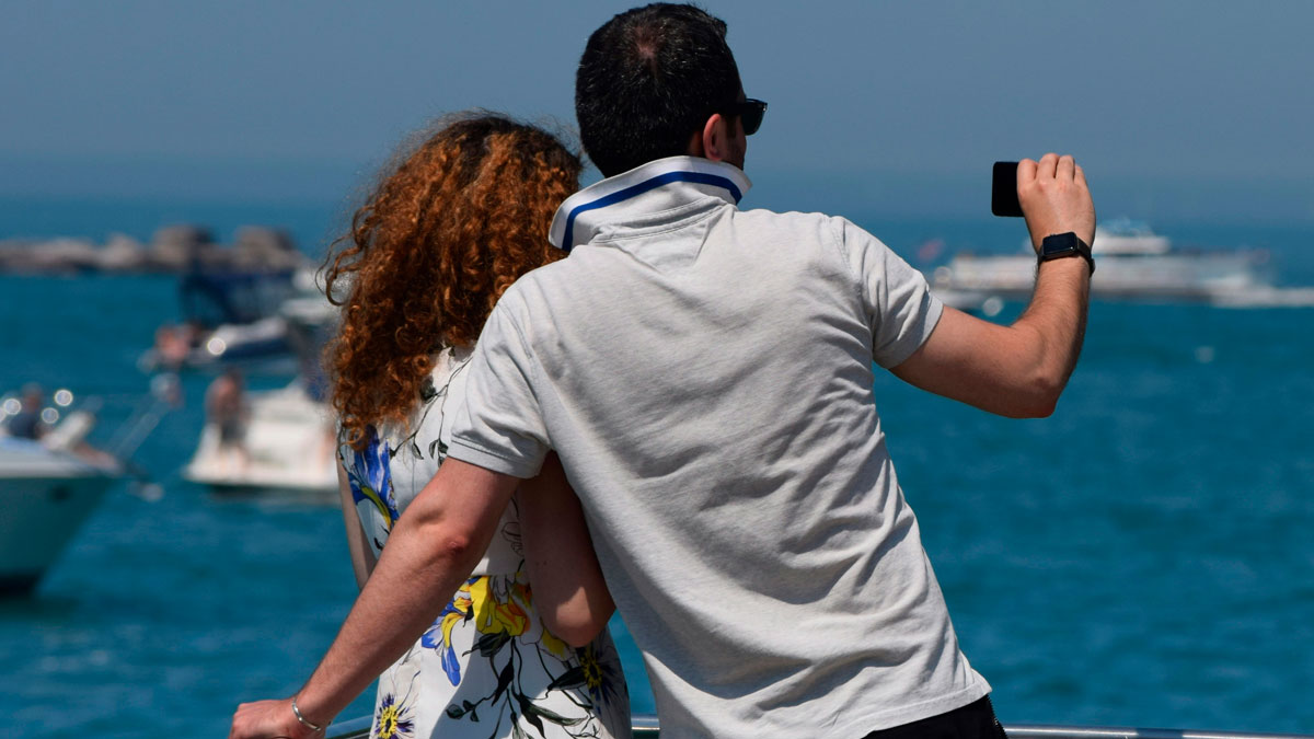 A couple by the sea taking a selfie, highlighting common performative behaviors people find frustrating in society.