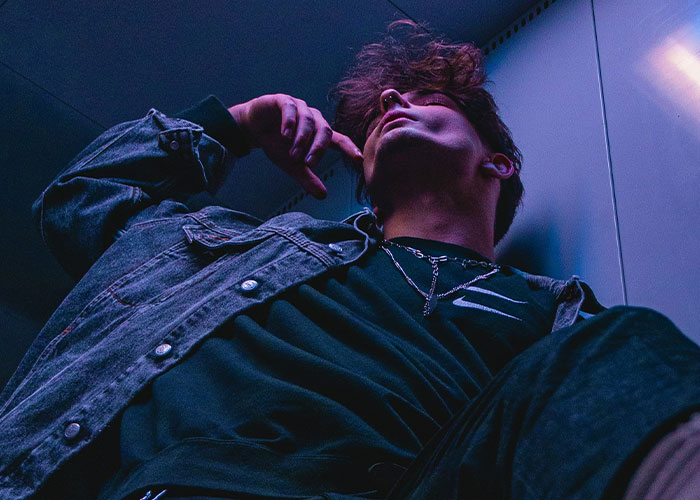 Young man in a dark room, wearing a denim jacket and necklace, representing quick reactions preventing a tragedy.