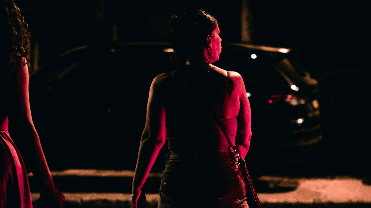 Woman walking at night with quick reactions preventing a tragedy, illuminated by dark red street lighting.
