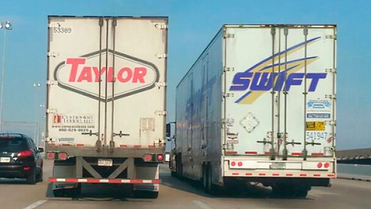 Two trucks side by side on highway with Taylor and Swift logos creating a rare coincidence on the road.
