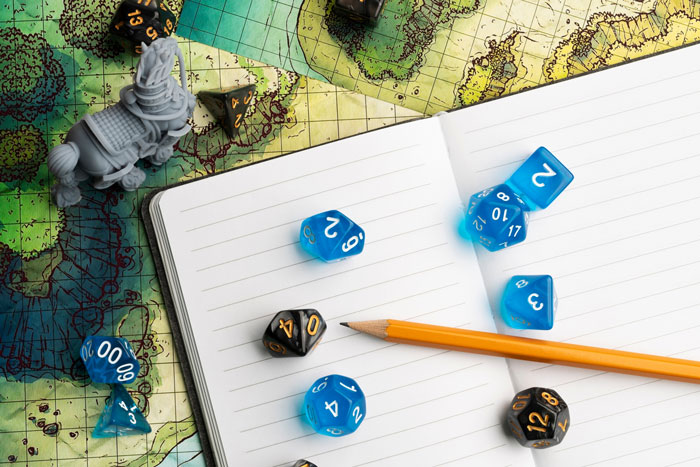 Blue and black dice with a pencil on an open notebook over a detailed fantasy game map and miniature figure. Blue and black dice with a pencil on an open notebook over a detailed fantasy game map and miniature figure.