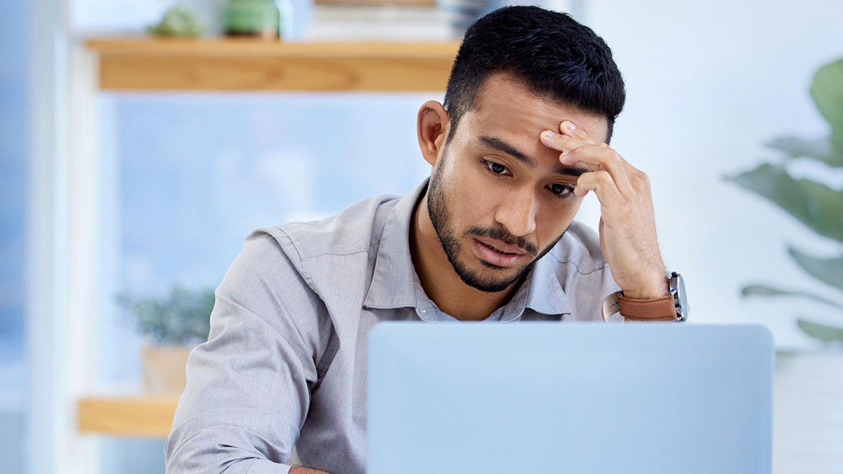 Indian guy looking concerned while working on laptop, reflecting on career risks of refusing to change name for US client.