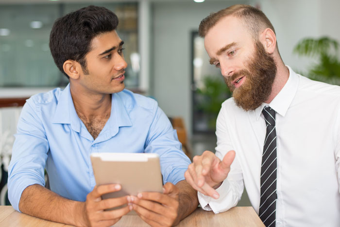 Indian guy in blue shirt discussing career risks with white colleague in office, refusing to change his name for US client. Indian guy in blue shirt discussing career risks with white colleague in office, refusing to change his name for US client.