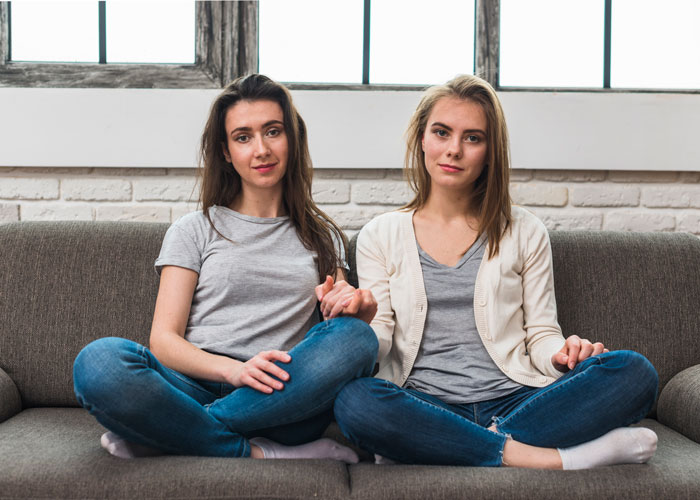 Two sisters sitting close on a couch, holding hands, showing a strong relationship between siblings and family.