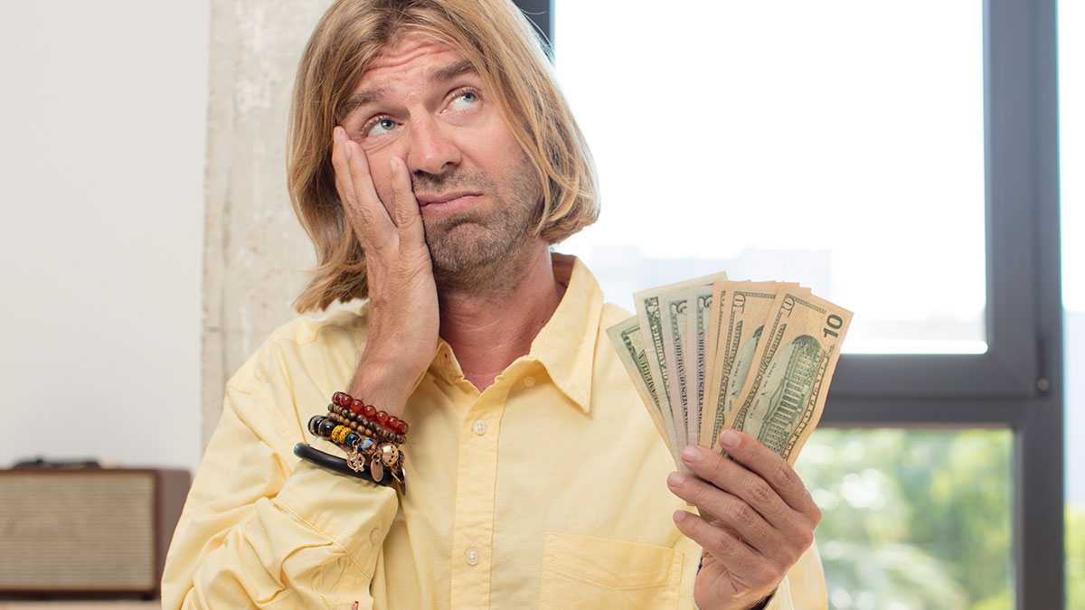 Man in a yellow shirt holding cash and looking puzzled, illustrating absurd things rich people spend money on.