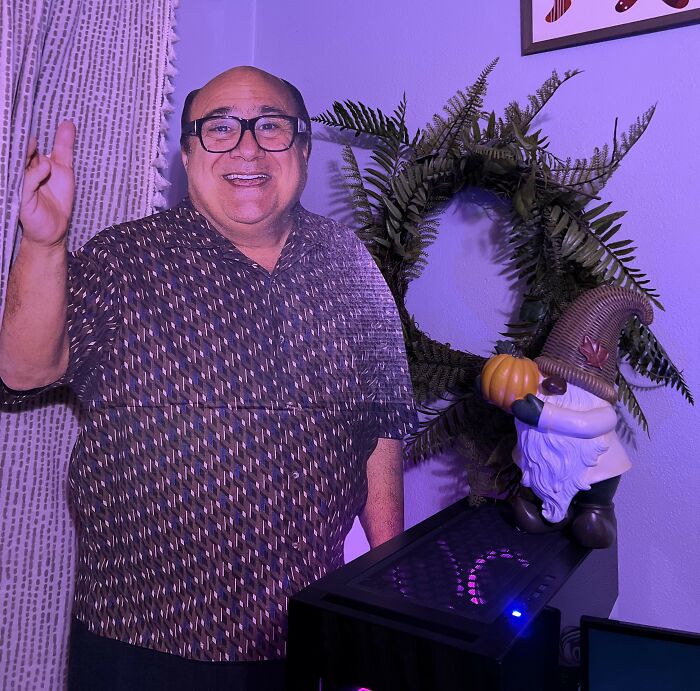 Cardboard cutout of a man smiling next to a gnome holding a pumpkin and a fern wreath in a home setting.