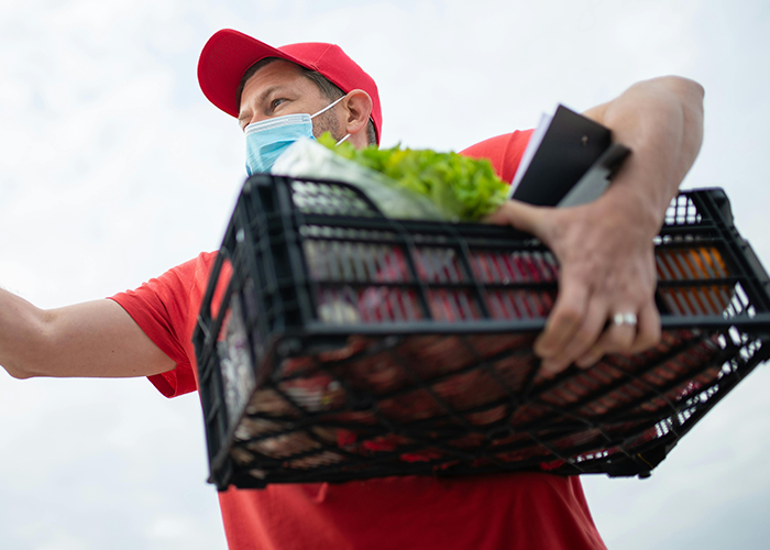 Instacart shopper wearing mask and red cap carrying groceries in a crate, highlighting customer demands and tips. Instacart shopper wearing mask and red cap carrying groceries in a crate, highlighting customer demands and tips.