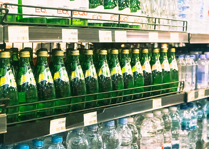 Rows of green glass and plastic water bottles on store shelves related to Instacart shopper carrying water demands tip Rows of green glass and plastic water bottles on store shelves related to Instacart shopper carrying water demands tip
