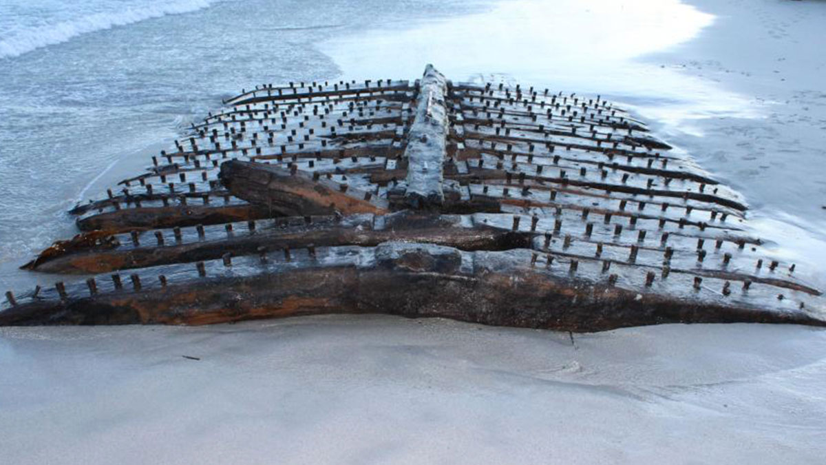 Rusty wooden shipwreck remains partially buried in sand on a beach with waves in the background at Sanday.