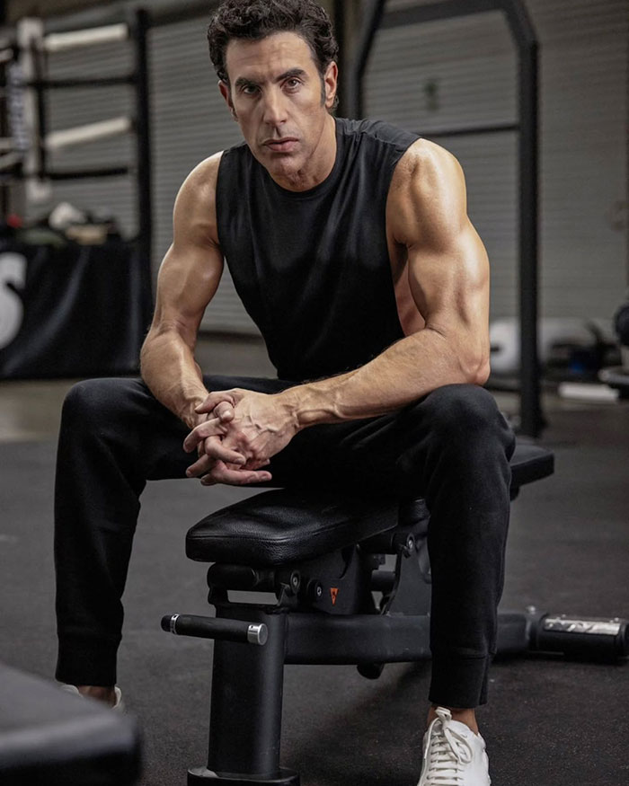 Man sitting on gym bench in a sleeveless black shirt showing muscular arms, related to Isla Fisher tough couple of years topic Man sitting on gym bench in a sleeveless black shirt showing muscular arms, related to Isla Fisher tough couple of years topic