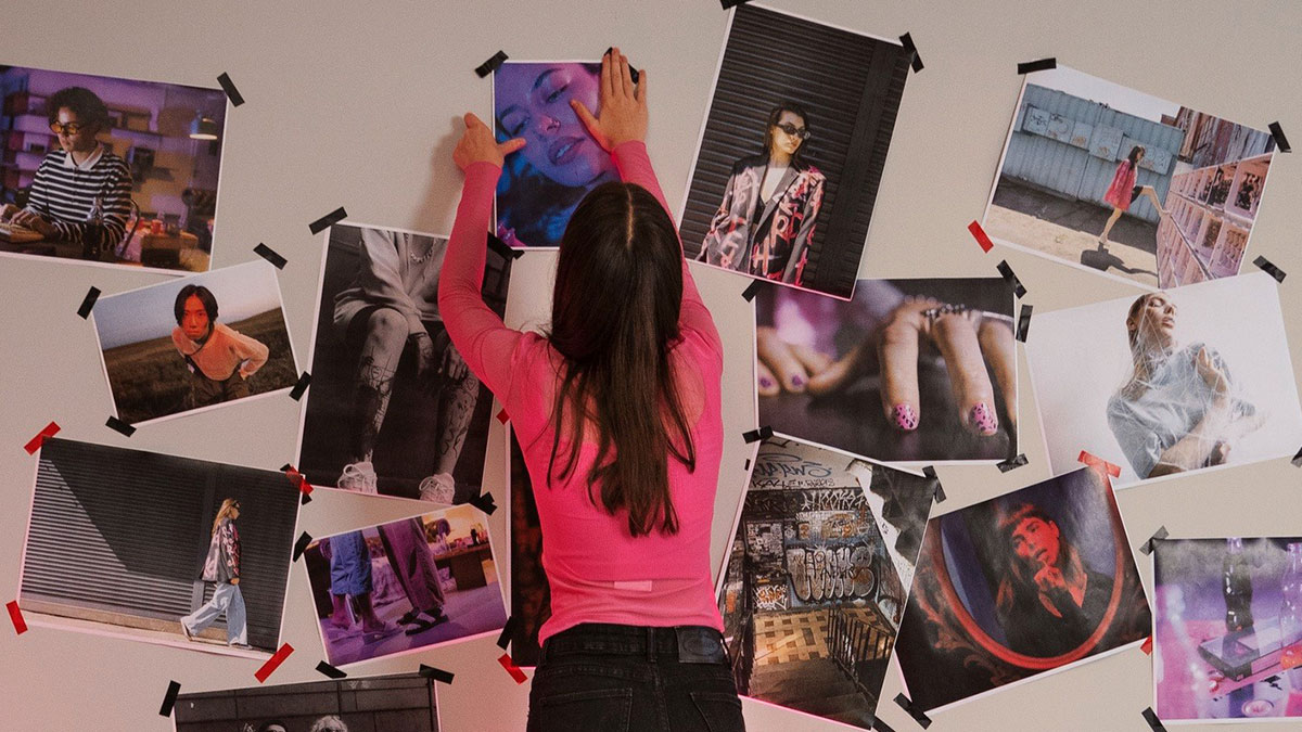 Woman in pink shirt arranging photos on wall, creating a mood board inspired by chilling true stories of scariest sounds at night