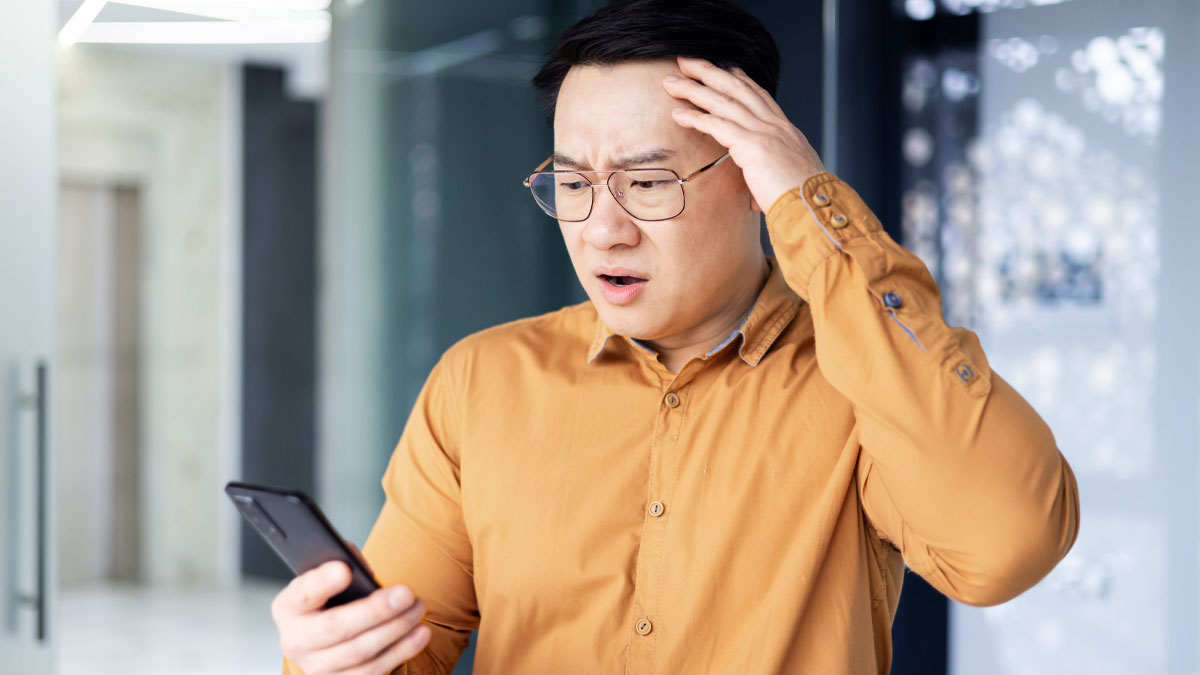 Man in glasses wearing a brown shirt looking shocked at his phone, illustrating terrifying true stories hard to believe.