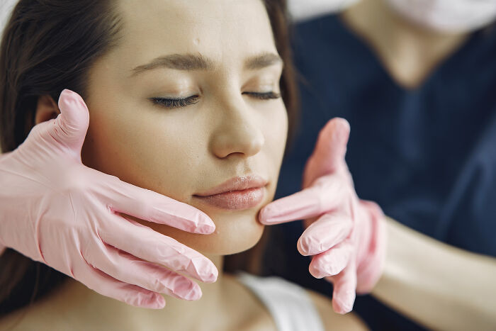 Close-up of a woman receiving facial treatment from a professional wearing pink gloves showing alpha vibe traits concept.