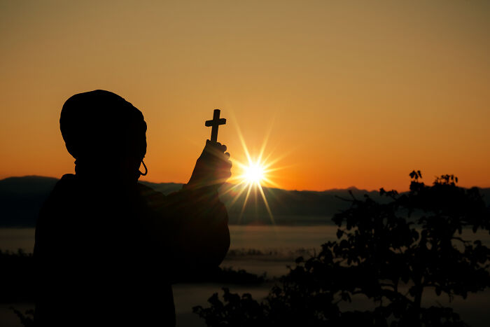 Silhouette of a person holding a cross against a sunrise, illustrating the whole alpha vibe and overcompensating traits concept.