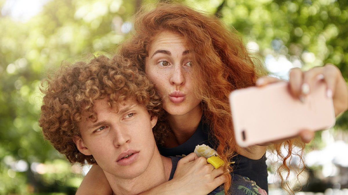 Young man and woman with curly hair taking a selfie outdoors, capturing the whole alpha vibe and overcompensating traits.
