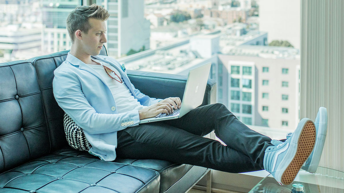 Man wins $14 million, wearing casual clothes while using a laptop and relaxing on a couch in a modern apartment.