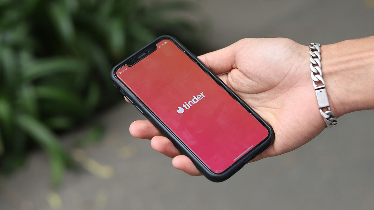 Hand holding smartphone with Tinder app loading screen, relating to NSFW stories shared online.