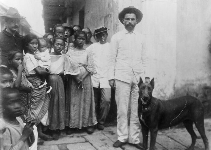 Group of Filipinos in traditional clothing with a man and dog on a street, showcasing the Philippines in the 1890s contrasts.