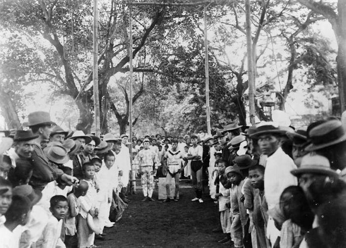 Crowd gathered outdoors under trees in the Philippines in the 1890s, showcasing cultural and historical contrasts.