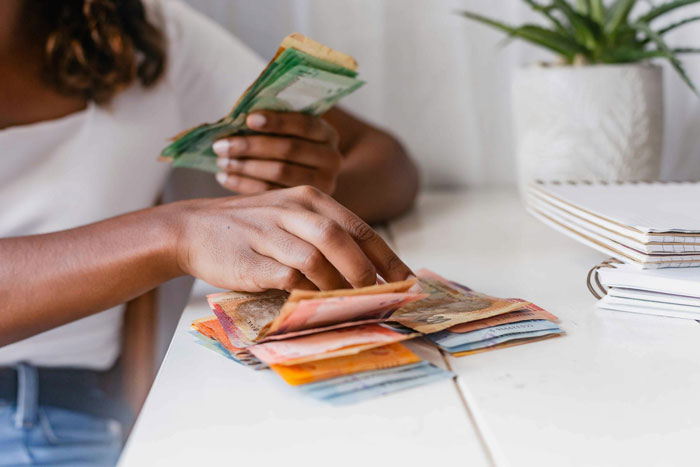 Woman counting money at table, illustrating babysitters earning a fair living wage discussion and reality check moment. Woman counting money at table, illustrating babysitters earning a fair living wage discussion and reality check moment.