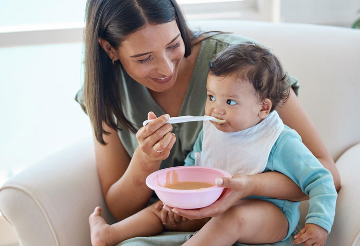 Young adult feeding toddler with a spoon, highlighting caregiving and feeding challenges in sibling responsibility. Young adult feeding toddler with a spoon, highlighting caregiving and feeding challenges in sibling responsibility.