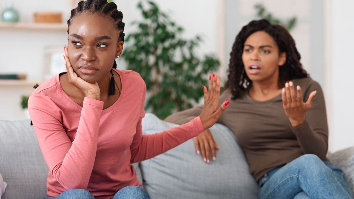Two women having a tense argument on a couch, one upset and refusing to listen, highlighting family money dispute issues.