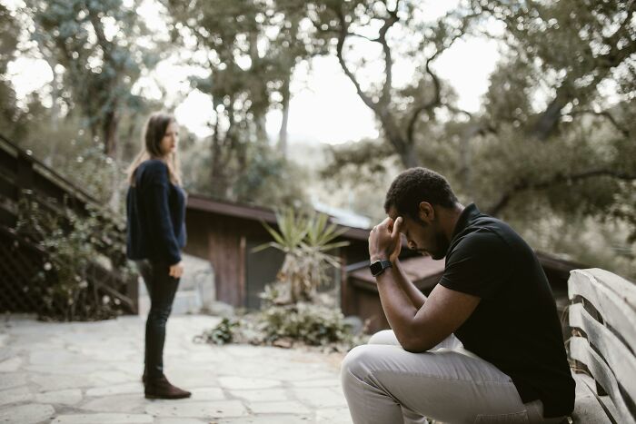 Man upset and sitting on bench while woman stands nearby outdoors, reflecting tension after brother swaps wife and kids. Man upset and sitting on bench while woman stands nearby outdoors, reflecting tension after brother swaps wife and kids.