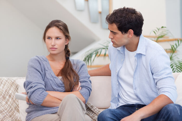 Brother and wife having tense conversation on couch, reflecting conflict after swapping family for new flame. Brother and wife having tense conversation on couch, reflecting conflict after swapping family for new flame.